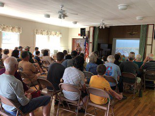 Community members sit in chairs in a large room to listen to a presentation.