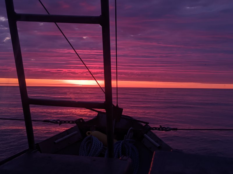 Steaming out to sea from Newburyport, MA at sunrise.... the sky is pink and orange and purple looking out over the bow of a fishing vessel as the sun rises