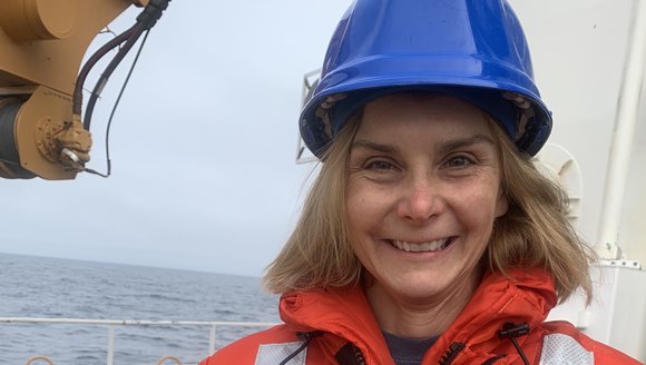 Dr. Janet Duffy-Anderson stands on deck of a boat in an orange jacket and blue helmet