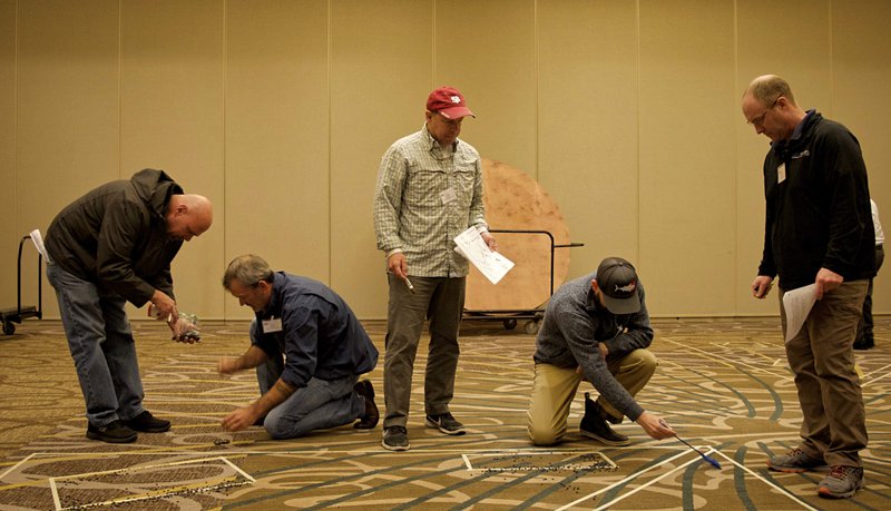 Six workshop participants are standing and sitting in a line in a large carpeted room.