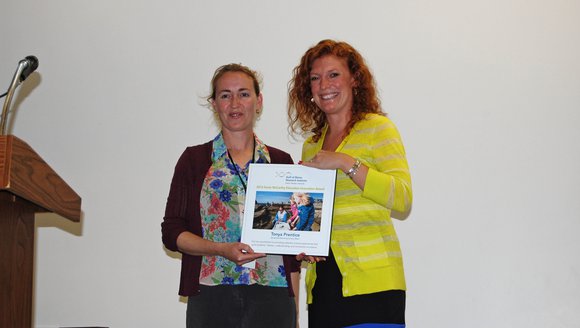 Woodstock Elementary School teacher Tonya Prentice holds up her McCarthy award in a flowery shirt, next to GMRI education staff member Meredyth Sullivan in a bright yellow shirt.