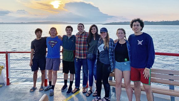 A group of undergraduates on a sunset cruise posing for the camera in front of a setting sun