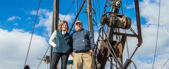 Fisheries Technical Assistance Program Manager Heather Cronin stands aboard a ship next to a fishermen, as they pose and smile for the camera.
