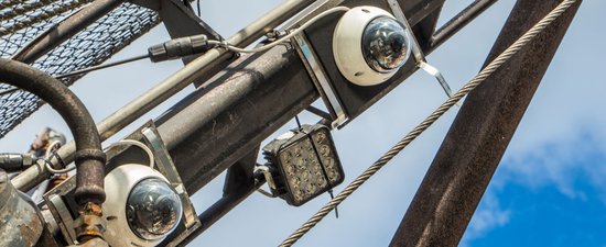 Two circular cameras with white bases and round lenses are mounted on a ship's beam that crosses the image frame diagonally from the bottom left of the image to the top right.