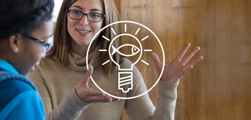 This image shows a white circle with a white outline of a lightbulb inside, centered in front of Sustainable Seafood Program Manager Kyle Foley in a brown shirt, engaging with a consumer.