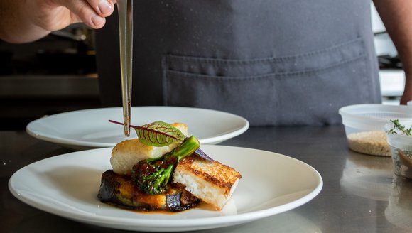 A chef placing a leaf on a seafood dish with tongs