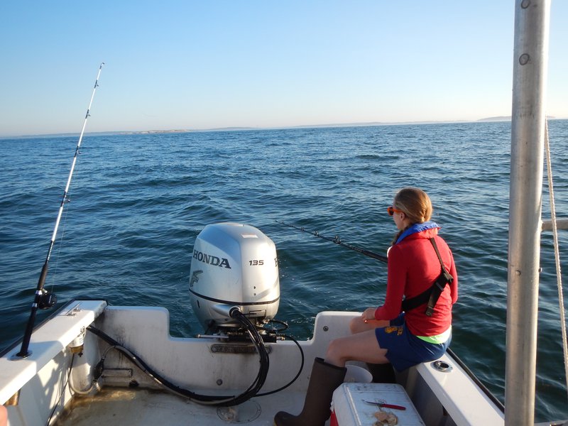 A woman in read uses a fishing pole off the back of a boat.