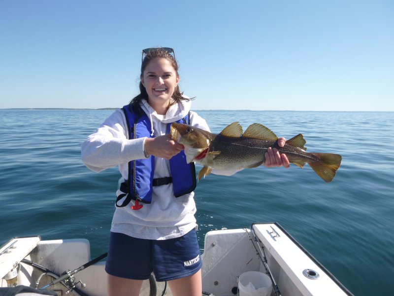 A woman holds up a large fish on a boat.