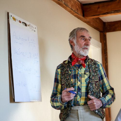Fishermen Chris Bean stands in front of a large white notepad in a yellow plaid shirt, with a floral vest, and a red bandana tied around his neck like a bowtie.