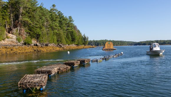 A white boat drifts on blue water next to a line of floating cages.