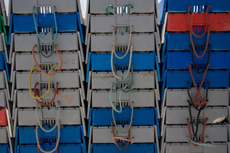 This is a close up photo showing three columns of stacked containers of varying colors, with handle ropes of different colors dangling downward in U-shapes.